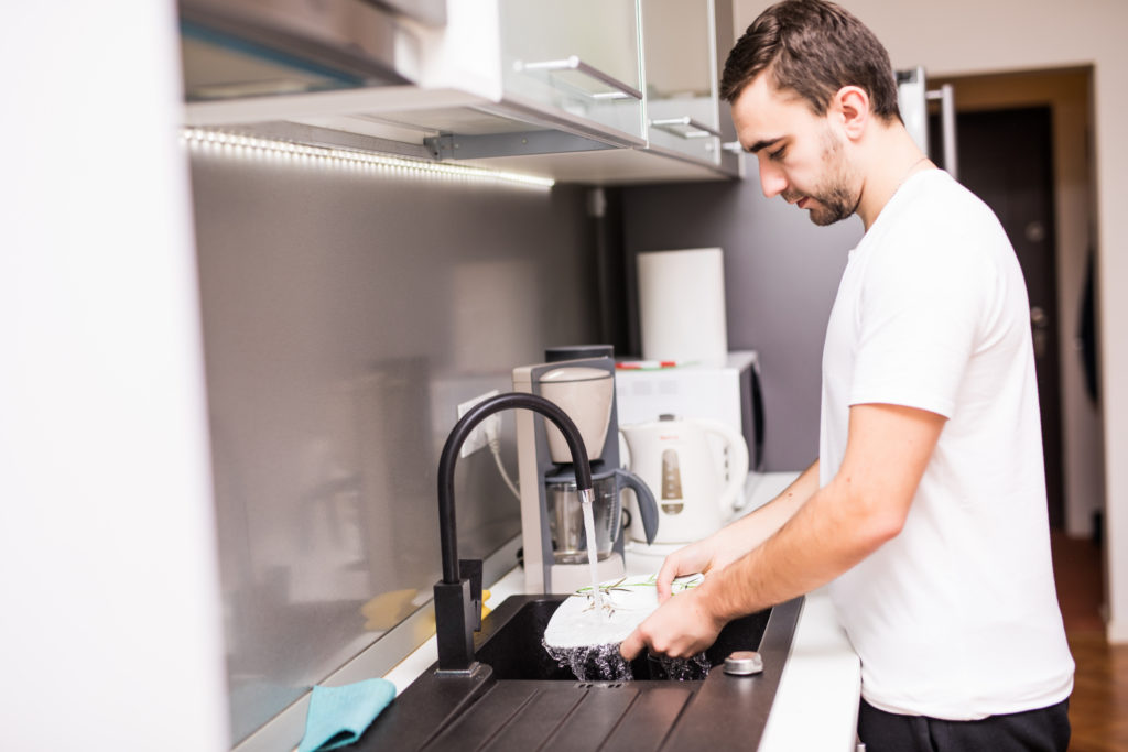 young happy man doing the dishes smiling confident and relaxed enjoying doing domestic work